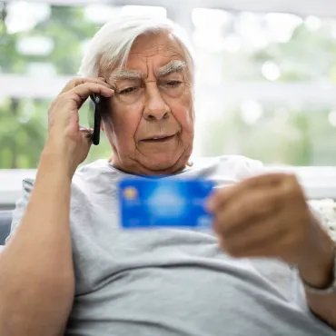 Bejaarde man met  bankkaart in de hand die aan het telefoneren is
